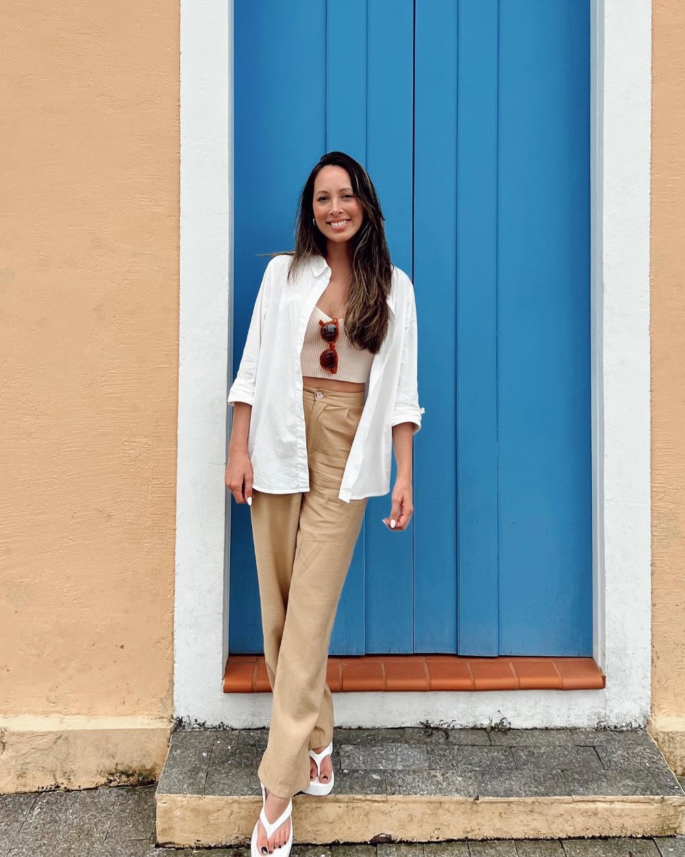 Flávia Zilli sorrindo em frente a uma porta azul, em Florianópolis
